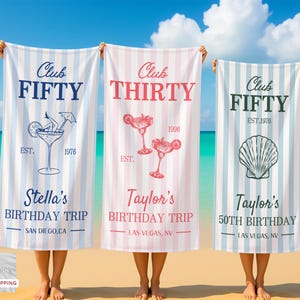 May include: Three beach towels with vertical stripes are held up on a beach. The towels have text and graphics. One says "Club FIFTY" with a cocktail graphic, another says "Club THIRTY" with cocktail graphics, and the last says "Club FIFTY" with a seashell graphic.