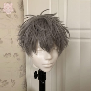 Peut inclure: Perruque grise avec une coupe courte et hérissée, présentée sur une tête de mannequin blanche. La perruque a une texture naturelle et est coiffée pour encadrer le visage. Le mannequin est monté sur un support noir sur fond blanc.