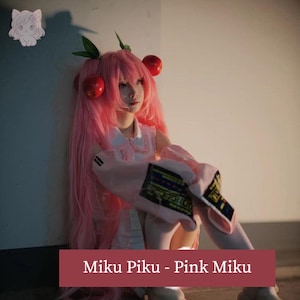 May include: A person in a pink cosplay outfit with long pink hair, red cherry hair accessories, and a white dress. The image includes the text "Miku Piku - Pink Miku" at the bottom.
