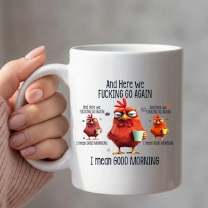 Può includere: Tazza in ceramica bianca con un design umoristico con tre polli dei cartoni animati e la scritta "And Here we Fucking Go Again. I mean Good Morning." I polli sono rossi e arancioni, con in mano delle tazze di caffè.