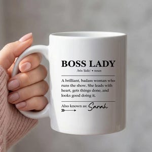Puede incluir: Taza de cerámica blanca con el texto "BOSS LADY" y una definición. La definición describe a una mujer brillante que dirige el espectáculo. La taza también incluye el nombre "Sarah".