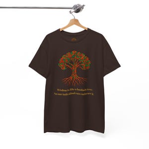Peut inclure: T-shirt marron avec un motif d'arbre stylisé aux accents rouges, verts et jaunes. Les racines et les branches de l'arbre sont richement détaillées. Le texte "Wisdom is like a baobab tree; No one individual can embrace it" est imprimé en dessous.