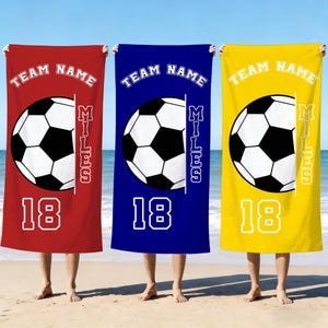 Op de afbeelding: Drie gepersonaliseerde voetbalhanddoeken in rood, blauw en geel. Elke handdoek heeft een voetbalafbeelding, de tekst "TEAM NAME", de naam "MILES" en het nummer "18" in het wit.