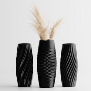 Puede incluir: Tres jarrones decorativos negros con texturas únicas. El jarrón central tiene un patrón de panal, mientras que los otros dos presentan un diseño en espiral. El jarrón central contiene hierba ornamental beige seca.