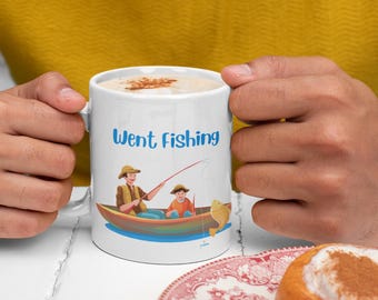 May include: White ceramic mug with the text "Went Fishing" in blue script. The mug features a cartoon illustration of two people fishing from a boat, with a fish jumping out of the water. The mug is held by a person.
