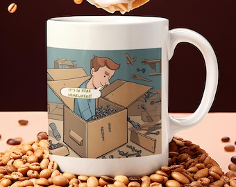May include: White ceramic coffee mug with a cartoon illustration of a person searching inside a box of tools. The text "IT'S IN HERE SOMEWHERE!" is in a speech bubble. The mug is surrounded by coffee beans.