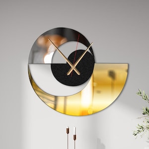 Puede incluir: Un reloj de pared moderno con un diseño único. El reloj presenta un acabado negro, dorado y espejado, con manecillas doradas y un centro circular negro. El reloj está montado en una pared gris claro, encima de una consola y una silla negras.