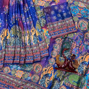 May include: A vibrant blue fabric featuring a multi-colored peacock and floral print with intricate geometric borders. The textile includes small reflective mirror accents throughout the pattern and is accompanied by two dark red swan figurines.