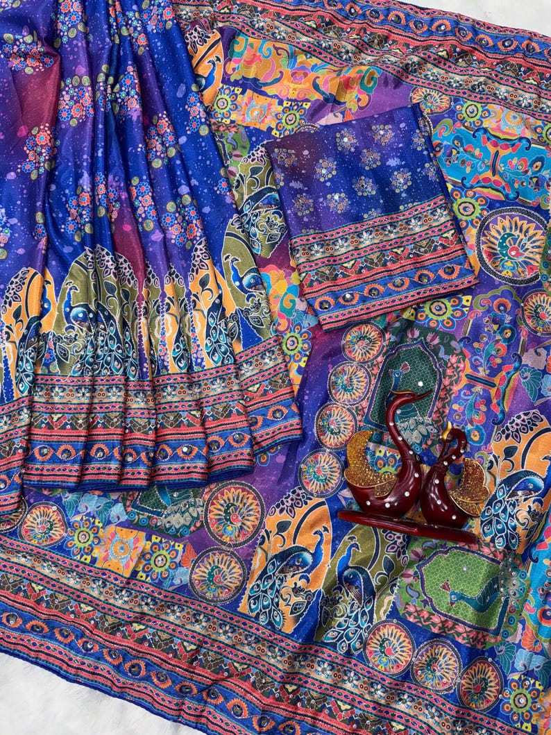 May include: A vibrant blue fabric featuring a multi-colored peacock and floral print with intricate geometric borders. The textile includes small reflective mirror accents throughout the pattern and is accompanied by two dark red swan figurines.
