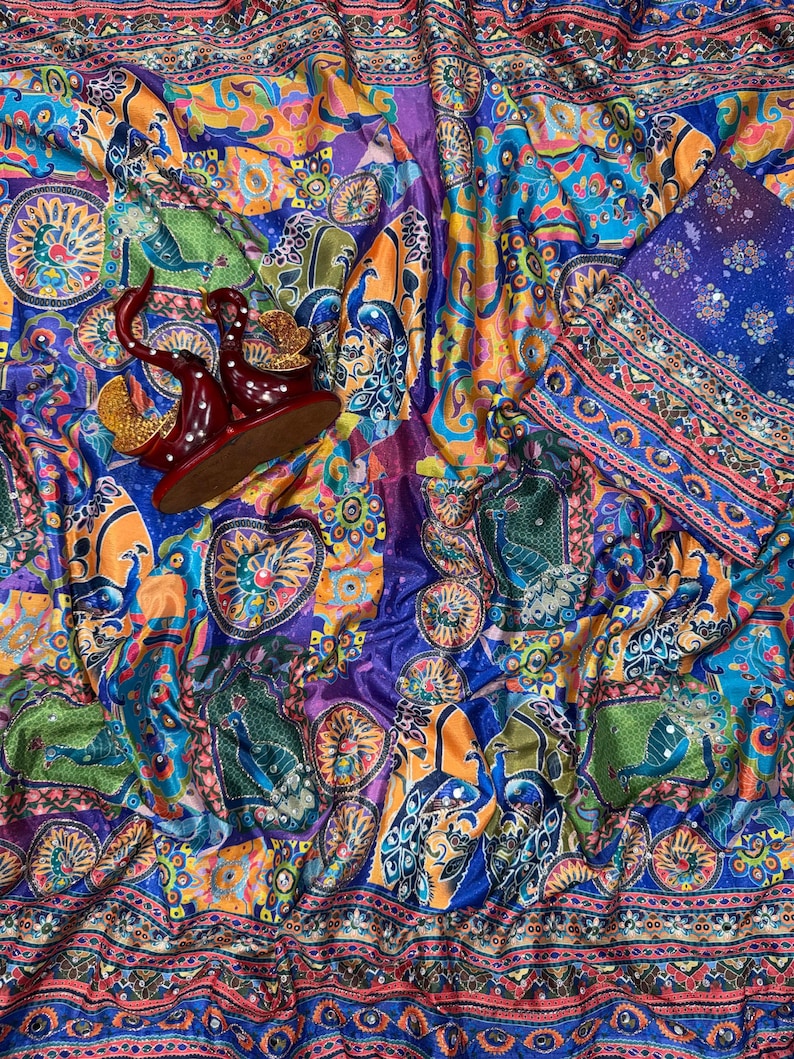 May include: A vibrant fabric featuring a multi-colored peacock and floral pattern in shades of blue, orange, and green. The textile includes a decorative border with geometric motifs and a pair of dark red, curved, swan-shaped ornaments.