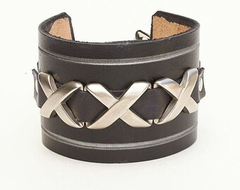 May include: A black leather cuff bracelet with a silver metal design. The design features a series of interlocking X shapes.