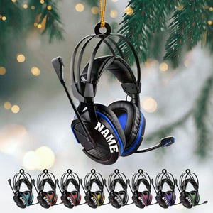 May include: Black and blue gaming headset ornament with the word "NAME" in white. The ornament is hanging from a gold string. Additional ornaments in various colors are displayed below the main ornament.