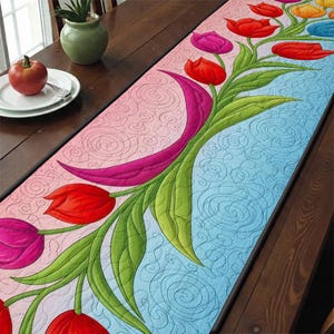 以下が含まれることがあります： チューリップの花柄が特徴のキルトテーブルランナー。ランナーはピンクと青の背景に渦巻き模様があります。チューリップは赤、ピンク、黄色で、緑の葉が付いています。