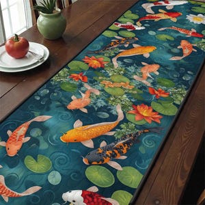 May include: A rectangular table runner featuring a koi pond design. The runner showcases orange, yellow, black, and white koi fish swimming among lily pads and orange lotus flowers on a teal background. The runner is placed on a wooden table.
