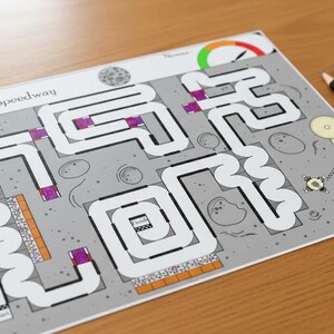 Op de afbeelding: Een bedrukt spelbord getiteld "MOON - Moon Speedway" met een doolhofontwerp, met een start- en finishgebied. Twee zwarte potloden en een witte gum liggen op een houten oppervlak.