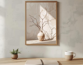 May include: A framed print featuring a beige vase with branches and buds. The vase sits on a surface, casting a shadow. The print is in a light brown wooden frame. A small potted plant and a mug are on the table.