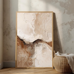 Puede incluir: Una obra de arte abstracta enmarcada con una paleta de colores neutros. La obra presenta un diseño texturizado con tonos beige, marrón y blanco, que recuerda a un paisaje. Una cesta de mimbre con una manta blanca está cerca.
