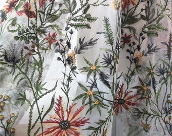 May include: Sheer white fabric with intricate floral embroidery. The design features a variety of flowers in shades of red, yellow, and green, along with detailed leaves and stems. The embroidery creates a delicate and textured appearance.