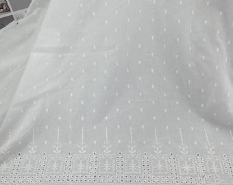 May include: White fabric with a delicate eyelet border and small dotted details. The fabric has a soft, flowing appearance, with the words "Flower Deals" visible in the upper left corner. This fabric is suitable for various sewing and crafting projects.