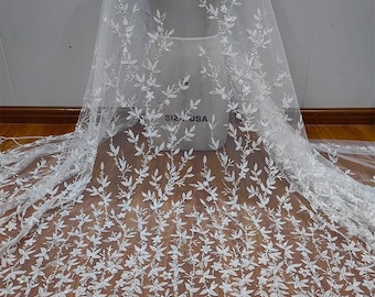 以下が含まれることがあります： 繊細な白いウェディングベール。複雑な花の刺繍が施されており、葉や小さな装飾が施された繊細なデザインで、質感のあるエレガントな外観を作り出しています。マネキンにかけられたベールは、生地の流れとデザインを示しています。「S12 USA」の文字が見えます。
