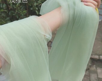May include: A sheer, light green fabric is held up in the air. The fabric is translucent and appears to be tulle or a similar material. The Chinese characters "浅绿色" are visible in the upper left corner.