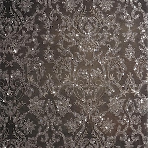 May include: Close-up of a dark gray fabric with an intricate floral and scrollwork pattern. The design is embellished with sparkling sequins, creating a shimmering effect. The fabric has a luxurious, elegant appearance.
