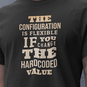 Può includere: T-shirt nero con la scritta "THE CONFIGURATION IS FLEXIBLE IF YOU CHANGE THE HARDCODED VALUE" in beige chiaro. La maglietta è realizzata in un materiale morbido e ha maniche corte.