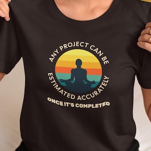 Pode incluir: Camiseta preta com um gráfico circular com uma figura meditando contra um pôr do sol. O texto diz: "QUALQUER PROJETO PODE SER ESTIMADO COM PRECISÃO APÓS A CONCLUSÃO."