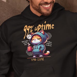 Pode incluir: Moletom preto com um gráfico de um gato usando um capuz e segurando uma xícara de café. O texto no moletom diz "99% uptime" e "1% LIFE". Texto adicional inclui "5th Coffee of the day" e "0 days without incidents".