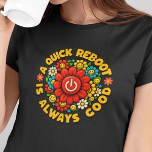Może przedstawiać: Czarna koszulka z kolorowym kwiatowym wzorem i napisem "A quick reboot is always good". Biały kubek z postacią z kreskówki jest trzymany przed twarzą.