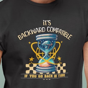 Puede incluir: Camiseta negra con un diseño de reloj de arena con un OVNI en su interior. El texto en la camiseta dice: "IT'S BACKWARD COMPATIBLE IF YOU GO BACK IN TIME."
