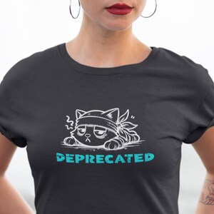 Op de afbeelding: Zwart T-shirt met een cartoonkat met een hoofdband en een chagrijnige uitdrukking. Het woord "DEPRECATED" staat in turquoise onder de kat. Het shirt heeft een ronde hals.
