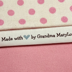 May include: White fabric with pink polka dots and a white label sewn on. The label says "Made with ♥ by Grandma MaryLou".