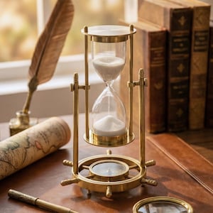 以下が含まれることがあります： 白い砂が詰まった透明なガラス室を備えた真鍮製の砂時計。砂時計は、コンパスのデザインが施された装飾的なベースに置かれています。 羽ペン、インク壺、丸められた地図も表示されています。