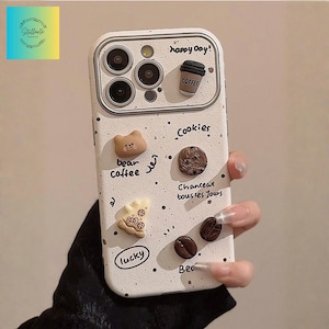 Könnte beinhalten: Eine weiße Handyhülle mit Kaffee- und Keksmotiven. Die Hülle zeigt Designs von Kaffeetasse, Bär, Keks und Kaffeebohnen. Der Text enthält "happy day!", "Cookies", "bean coffee", "Chanceux tous les Jours", "lucky" und "Beo".