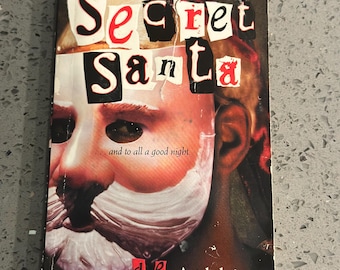 Puede incluir: Un libro de bolsillo titulado "Secret Santa" de d.e. Athkins. La portada presenta una cara con barba de Papá Noel y el texto "Secret Santa" en un estilo collage. El libro está publicado por Scholastic.