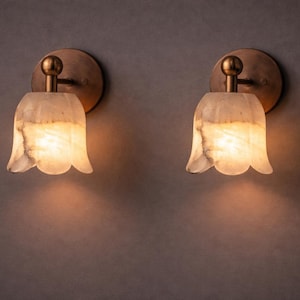 Modern brass wall sconce set with alabaster stone shade, minimalist bedroom wall lighting on grey background Mid century brass wall lights with white alabaster tulip shades, luxury wall sconce pair for bedroom decor Set of two brass wall sconces with natural alabaster shades, elegant modern wall lighting fixture Minimal brass wall lamps with alabaster shade, bedside wall lighting pair on neutral grey wall Luxury brass wall sconce pair with alabaster tulip glass shade, modern wall lighting.