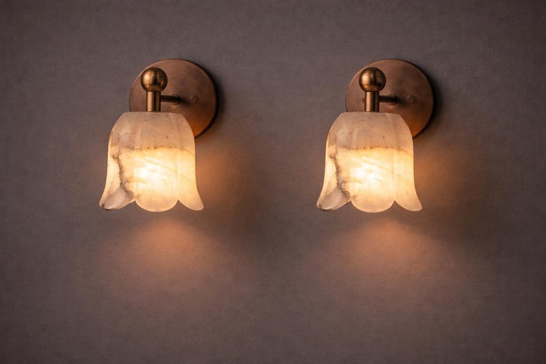 Modern brass wall sconce set with alabaster stone shade, minimalist bedroom wall lighting on grey background Mid century brass wall lights with white alabaster tulip shades, luxury wall sconce pair for bedroom decor Set of two brass wall sconces with natural alabaster shades, elegant modern wall lighting fixture Minimal brass wall lamps with alabaster shade, bedside wall lighting pair on neutral grey wall Luxury brass wall sconce pair with alabaster tulip glass shade, modern wall lighting.