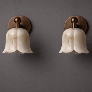 Modern brass wall sconce set with alabaster stone shade, minimalist bedroom wall lighting on grey background Mid century brass wall lights with white alabaster tulip shades, luxury wall sconce pair for bedroom decor Set of two brass wall sconces with natural alabaster shades, elegant modern wall lighting fixture Minimal brass wall lamps with alabaster shade, bedside wall lighting pair on neutral grey wall Luxury brass wall sconce pair with alabaster tulip glass shade, modern wall lighting.