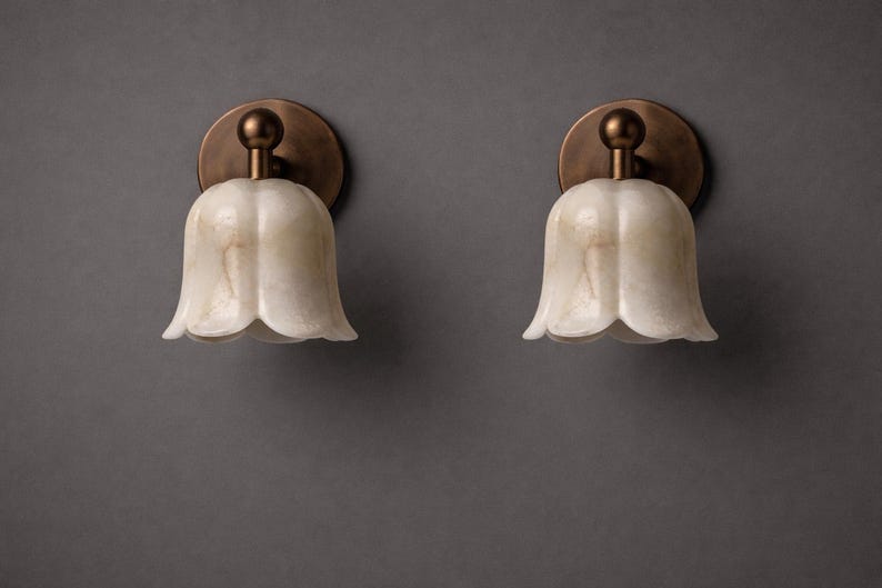 Modern brass wall sconce set with alabaster stone shade, minimalist bedroom wall lighting on grey background Mid century brass wall lights with white alabaster tulip shades, luxury wall sconce pair for bedroom decor Set of two brass wall sconces with natural alabaster shades, elegant modern wall lighting fixture Minimal brass wall lamps with alabaster shade, bedside wall lighting pair on neutral grey wall Luxury brass wall sconce pair with alabaster tulip glass shade, modern wall lighting.