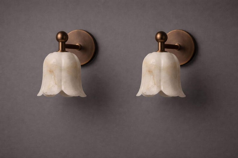 Modern brass wall sconce set with alabaster stone shade, minimalist bedroom wall lighting on grey background Mid century brass wall lights with white alabaster tulip shades, luxury wall sconce pair for bedroom decor Set of two brass wall sconces with natural alabaster shades, elegant modern wall lighting fixture Minimal brass wall lamps with alabaster shade, bedside wall lighting pair on neutral grey wall Luxury brass wall sconce pair with alabaster tulip glass shade, modern wall lighting.