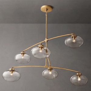 May include: A contemporary chandelier featuring six clear glass globe shades. The fixture has a gold-coloured metal frame and a central stem for ceiling mounting. Each globe houses a single light bulb.