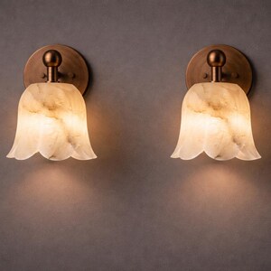 Modern brass wall sconce set with alabaster stone shade, minimalist bedroom wall lighting on grey background Mid century brass wall lights with white alabaster tulip shades, luxury wall sconce pair for bedroom decor Set of two brass wall sconces with natural alabaster shades, elegant modern wall lighting fixture Minimal brass wall lamps with alabaster shade, bedside wall lighting pair on neutral grey wall Luxury brass wall sconce pair with alabaster tulip glass shade, modern wall lighting.