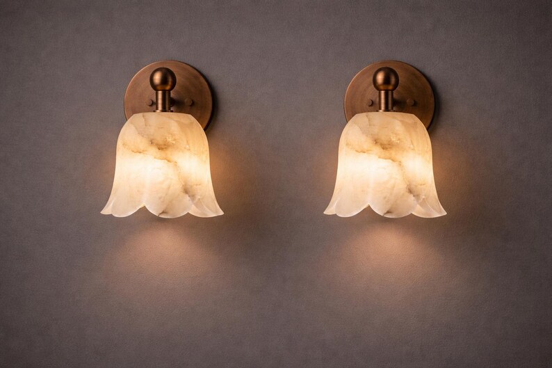 Modern brass wall sconce set with alabaster stone shade, minimalist bedroom wall lighting on grey background Mid century brass wall lights with white alabaster tulip shades, luxury wall sconce pair for bedroom decor Set of two brass wall sconces with natural alabaster shades, elegant modern wall lighting fixture Minimal brass wall lamps with alabaster shade, bedside wall lighting pair on neutral grey wall Luxury brass wall sconce pair with alabaster tulip glass shade, modern wall lighting.