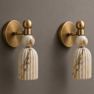 May include: Two wall sconces with a brass finish and a marble-like, cream-coloured shade with brown veining. The sconces have a round base and a decorative, ribbed design on the shade. The overall design is elegant and suitable for interior lighting.