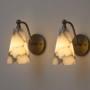 May include: Two wall sconces with a marble-like, cone-shaped shade. The shades are white with gray veining, and the fixtures have a bronze finish. The sconces are mounted on round bronze backplates and have a curved arm.