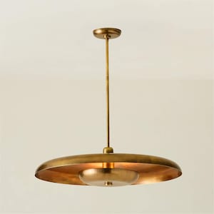 Könnte beinhalten: Eine messingfarbene Pendelleuchte im Mid-Century-Modern-Stil. Sie hat eine lange, schlanke Stange, die an einer kreisförmigen Deckenbefestigung befestigt ist. Ein großer, flacher, scheibenförmiger Schirm hängt darunter, darunter eine kleinere, runde Lichtquelle.