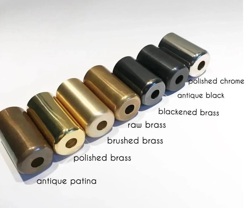 May include: A collection of cylindrical metal objects in various finishes, including antique patina, polished brass, brushed brass, raw brass, blackened brass, antique black, and polished chrome. Each cylinder has a hole at both ends, and the names of the finishes are labeled.