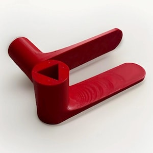 Può includere: Un utensile in plastica rosso brillante con un foro triangolare e due bracci estesi. L'utensile è progettato con una base cilindrica e una finitura liscia e lucida. I bracci hanno una forma leggermente curva.