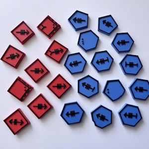 Puede incluir: Vista aérea de piezas de juego cuadradas rojas y hexagonales azules. Cada pieza presenta un diseño de flecha negra. Las piezas están dispuestas sobre una superficie blanca, creando un patrón. Tema de juego de mesa.